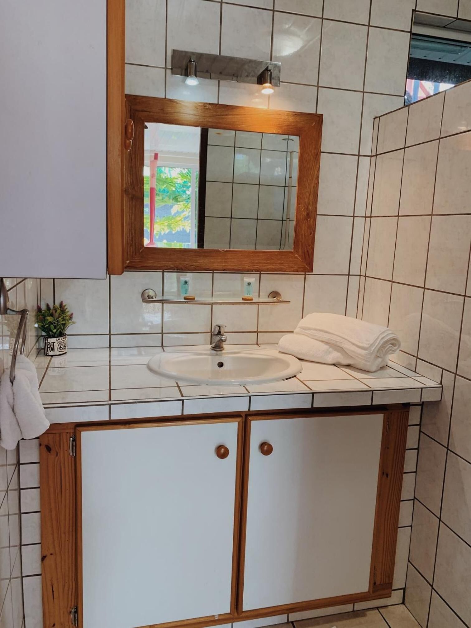 Ein Badezimmer mit weißem Waschbecken, Holzschränken, einem Spiegel und einem Handtuchhalter.