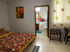 A bedroom with a bed, a chair, a bathroom visible through an open door, and a painting on the wall. - City Home Tahiti (Papeete)