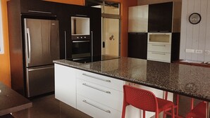A modern kitchen with a stainless steel refrigerator, a built-in oven, and a microwave. There are white cabinets and a granite countertop. - City Home Tahiti (Papeete)