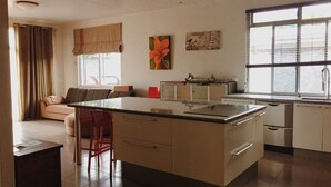A modern kitchen with a central island, a dining area with a sofa and chairs, and a large window providing natural light. - City Home Tahiti (Papeete)