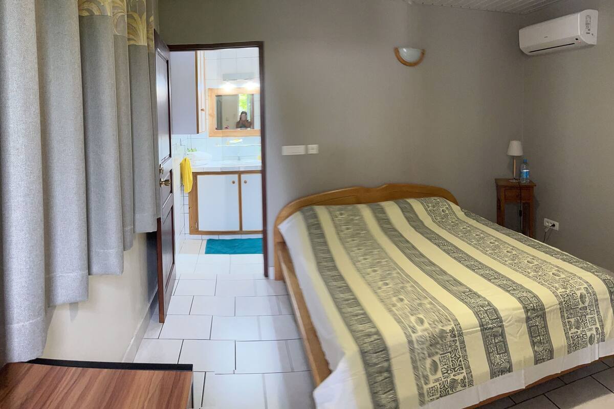 A bedroom with a bed, a bedside table, a mirror, and an air conditioning unit.