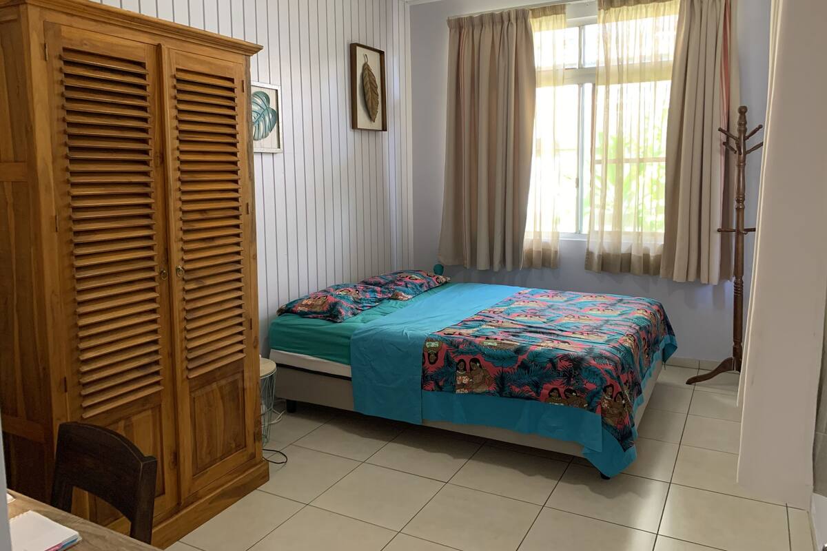 A room with a bed, a wardrobe, a window with curtains, and a coat rack.