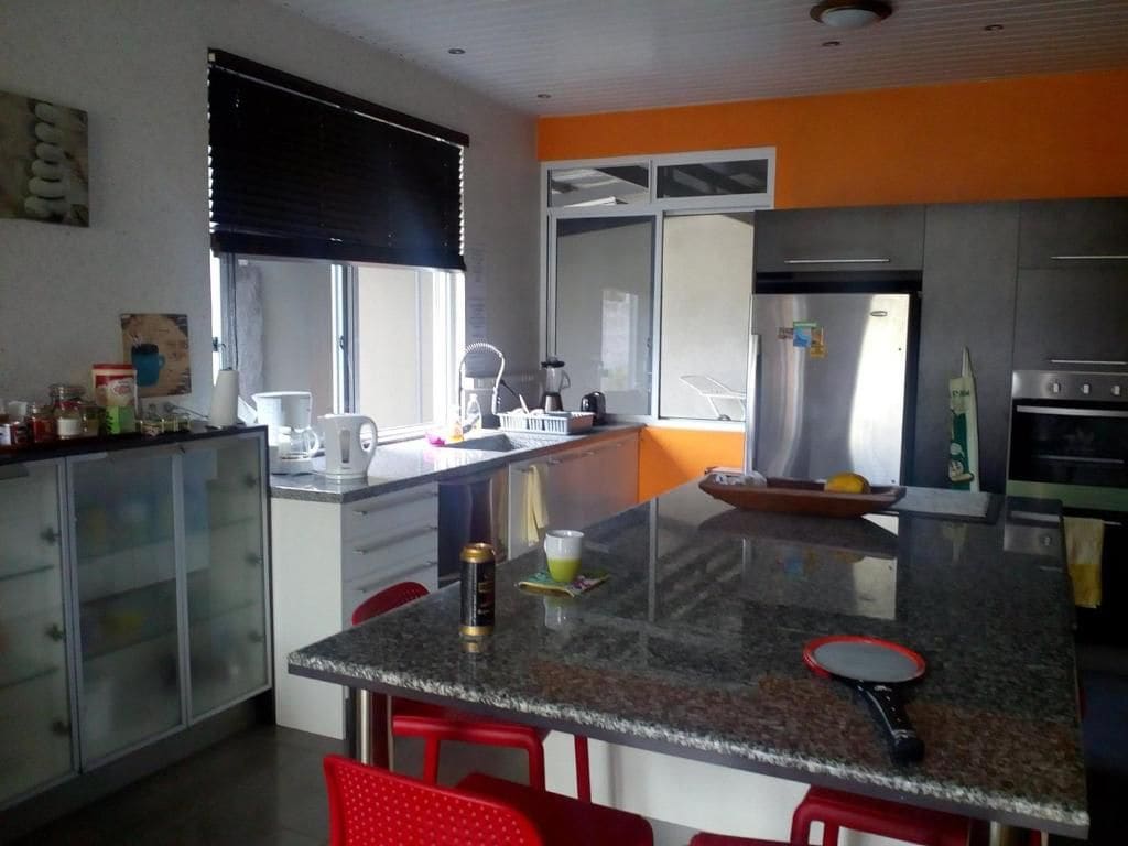 A modern kitchen with a central island, red bar stools, and a large window.