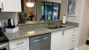 Una cucina moderna con mobili bianchi, un piano di lavoro in granito, un lavello in acciaio inossidabile e una lavastoviglie.