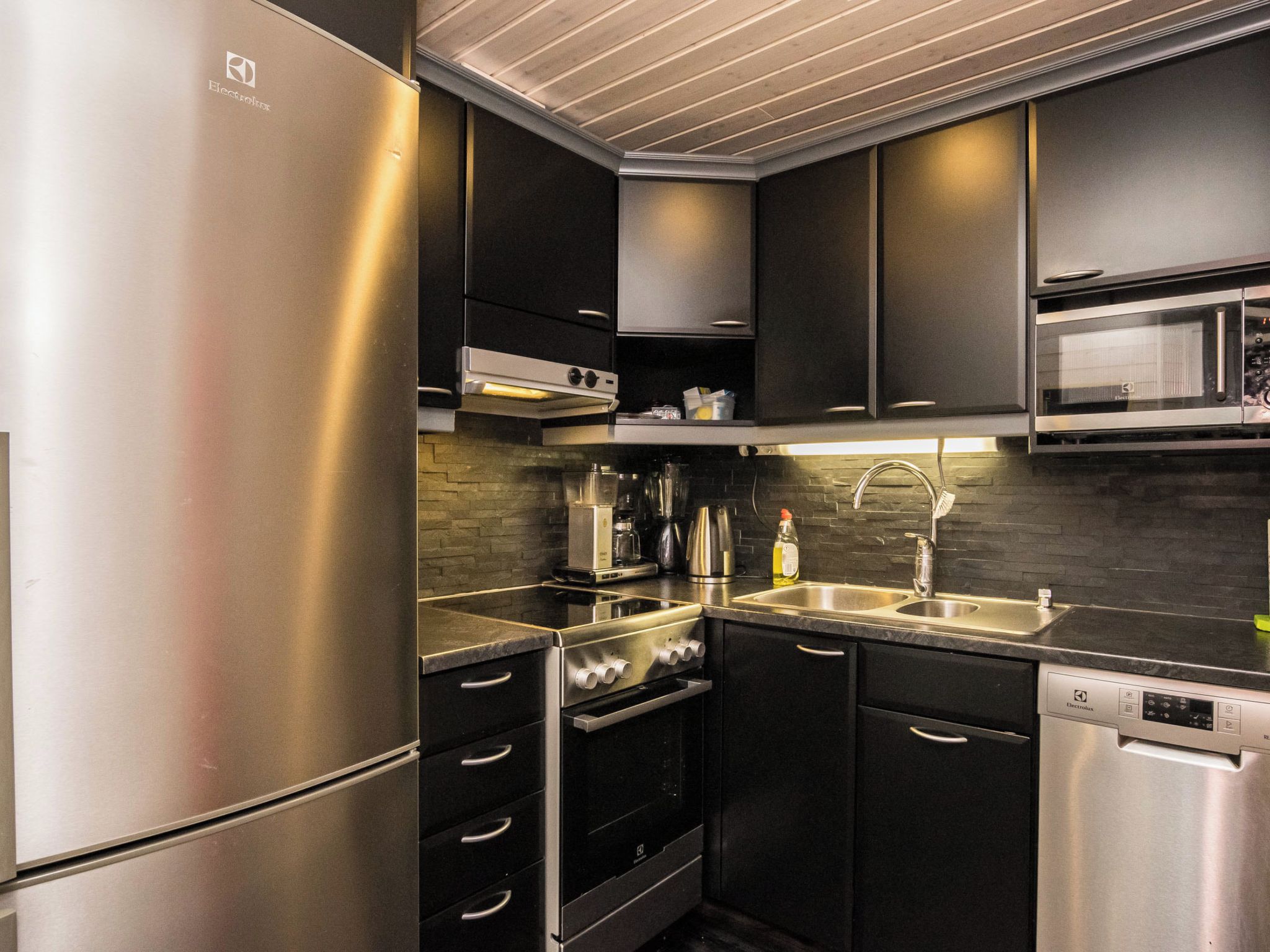 A modern kitchen with stainless steel appliances, black cabinetry, and a tiled backsplash.