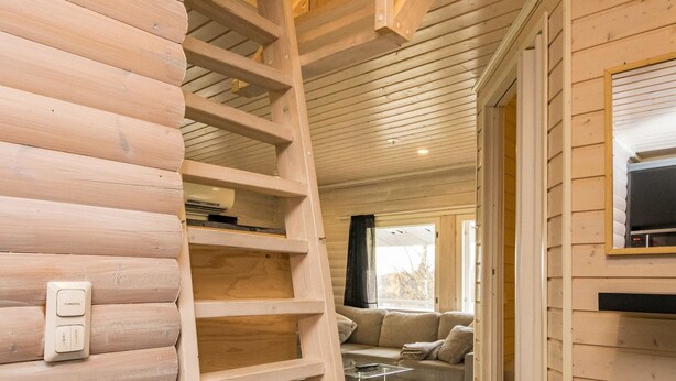A wooden interior with a wooden ladder, a sofa, and a TV mounted on the wall.