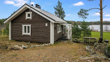 Un piccolo chalet in legno con veranda, un camino e vista libera su un lago sullo sfondo.