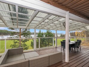 A covered outdoor deck with a view of a lake and forest.