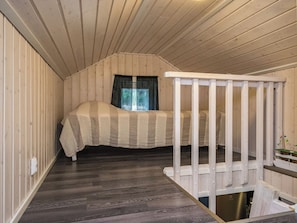 Une chambre à coucher avec un lit, une fenêtre avec des rideaux, un plancher en bois et une rambarde blanche.