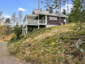 Une maison à deux étages dotée d’un balcon, située sur une colline, avec un chemin de gravier menant à l’entrée.
