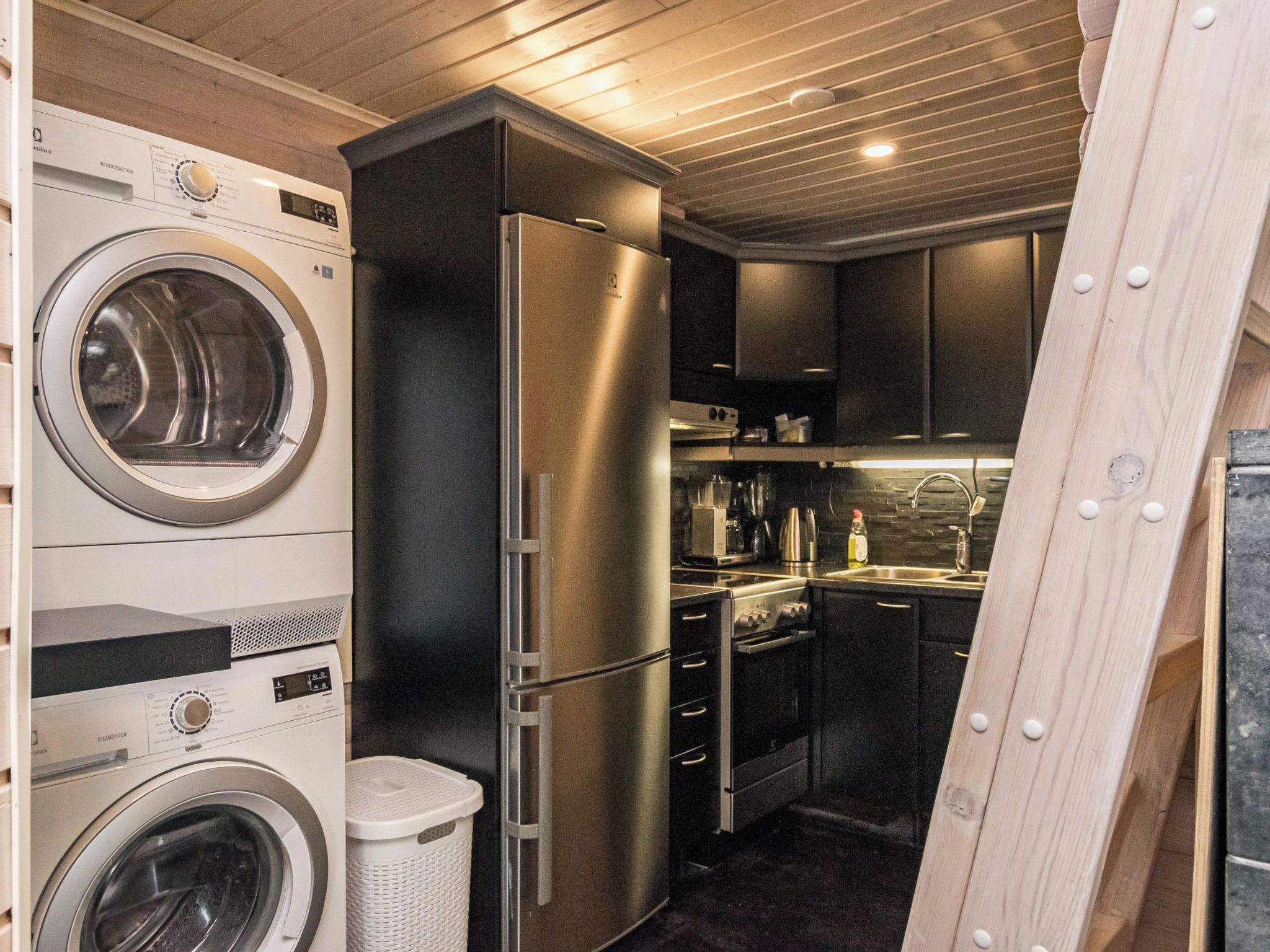 A compact kitchen with a stainless steel refrigerator, a washing machine, and a sink.