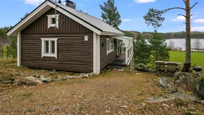 A rustic cabin with a porch, a small deck, and a view of a lake.