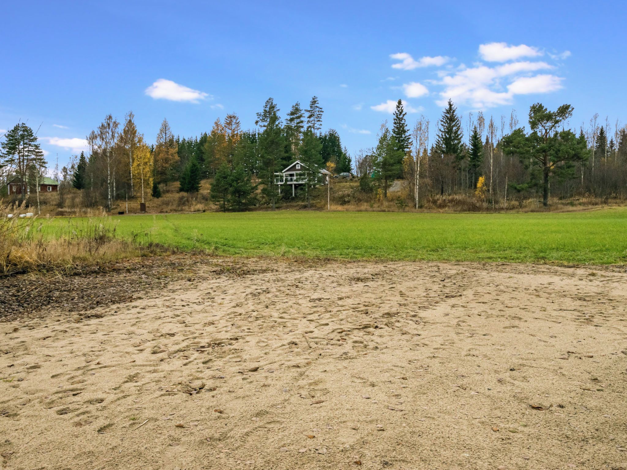 Zona arenosa con un campo verde y una casa al fondo.