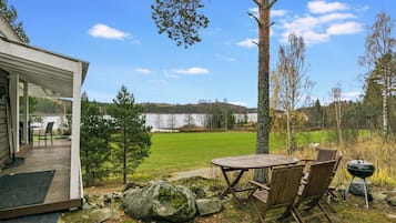 A covered patio with outdoor furniture, a view of a lake, and a forested area in the background.