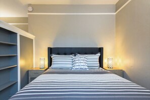 A neatly arranged bedroom with a striped bedspread, a tufted headboard, and two bedside lamps.