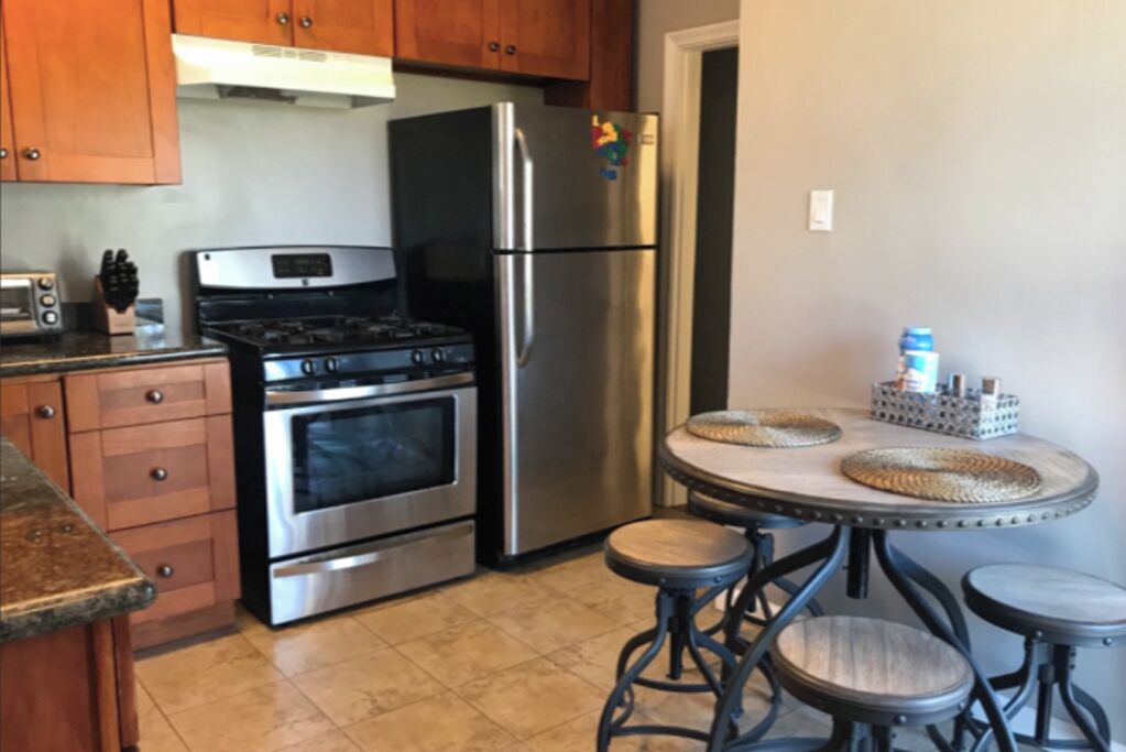 A kitchen with wooden cabinets, stainless steel appliances, a gas stove, an oven, a refrigerator, and a round table with stools.
