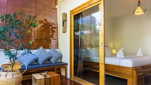 A room with a wooden bench, a glass door leading to a balcony, and a bed with white bedding and towels. - Focus Rooms (El Nido)