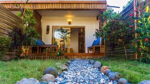 A pathway leading to a wooden structure with a glass door, surrounded by lush greenery and a bamboo fence. - Focus Rooms (El Nido)
