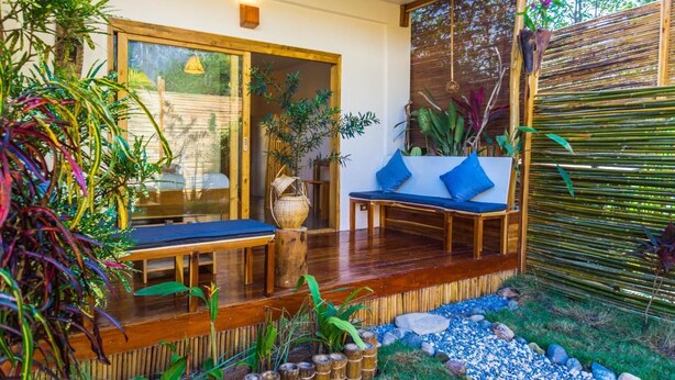 A wooden deck with a bench and a table, surrounded by bamboo plants and a bamboo fence. - Focus Rooms (El Nido)