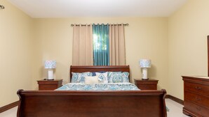 Un dormitorio con una cama de madera, dos mesitas de noche con lámparas, un aparador y una ventana con cortinas.
