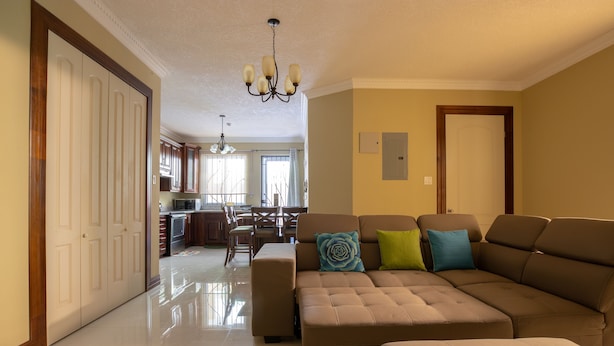 Una sala de estar amplia con un sofá seccional grande, una zona de comedor y una cocina al fondo, con un candelabro.