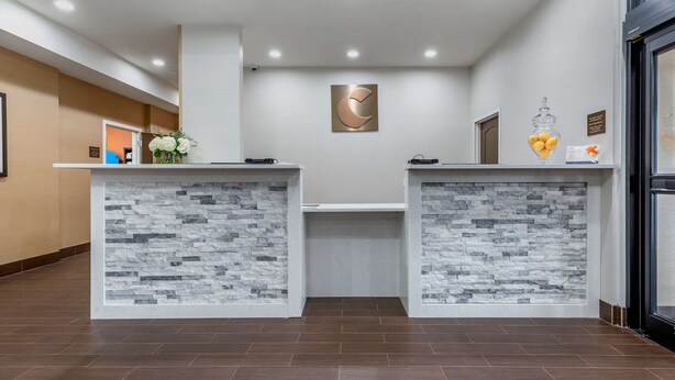 A reception area with two counters, a clock on the wall, and a flower arrangement. - Comfort Inn Brewster (Brewster)