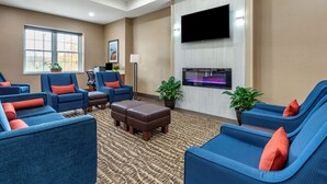 A hotel lobby with blue sofas, a brown ottoman, a flat-screen TV, and a large window. - Comfort Inn Brewster (Brewster)