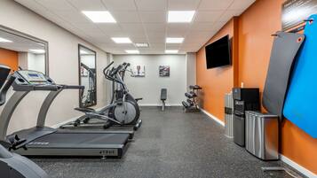 Un gimnasio con cintas de correr, una elíptica, una banca, un dispensador de agua y un televisor en la pared.
