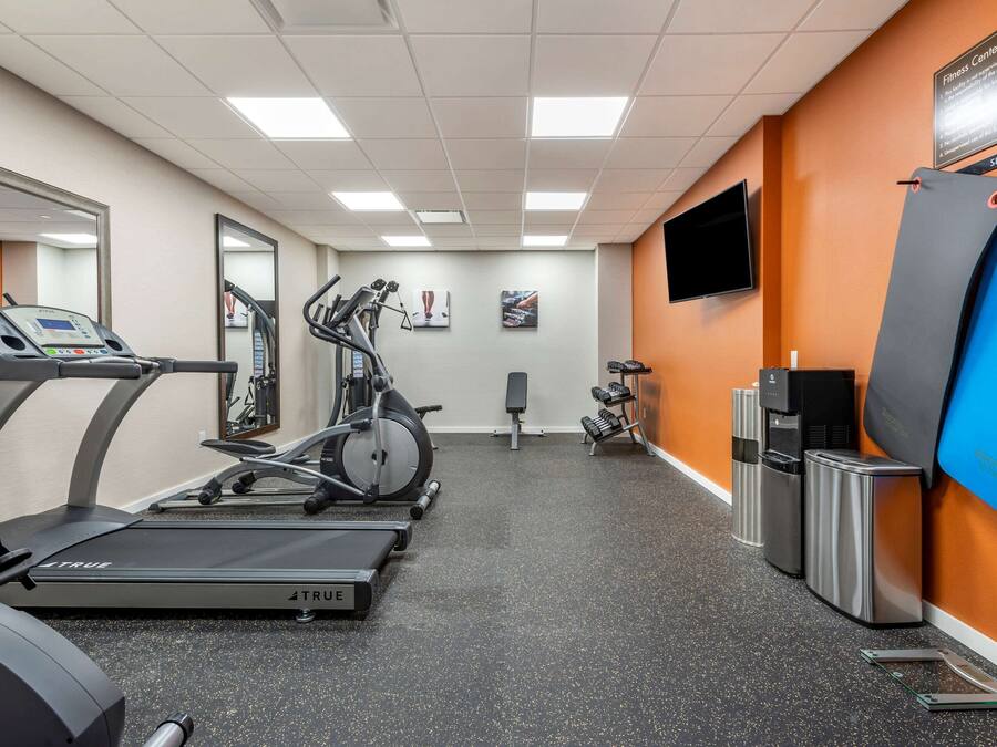 Une salle de sport équipée de tapis de course, d’un vélo elliptique, d’un banc de musculation, d’un distributeur d’eau et d’un téléviseur fixé au mur.