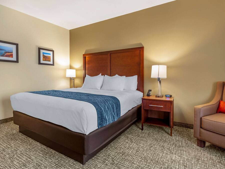 A hotel room with a large bed, two bedside lamps, a nightstand, a chair, and two framed pictures on the wall.
