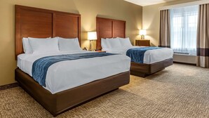 A hotel room with two beds, each with a wooden headboard, white linens, and a blue throw blanket. There are two bedside tables with lamps, and a large window with curtains. - Comfort Inn Brewster (Brewster)