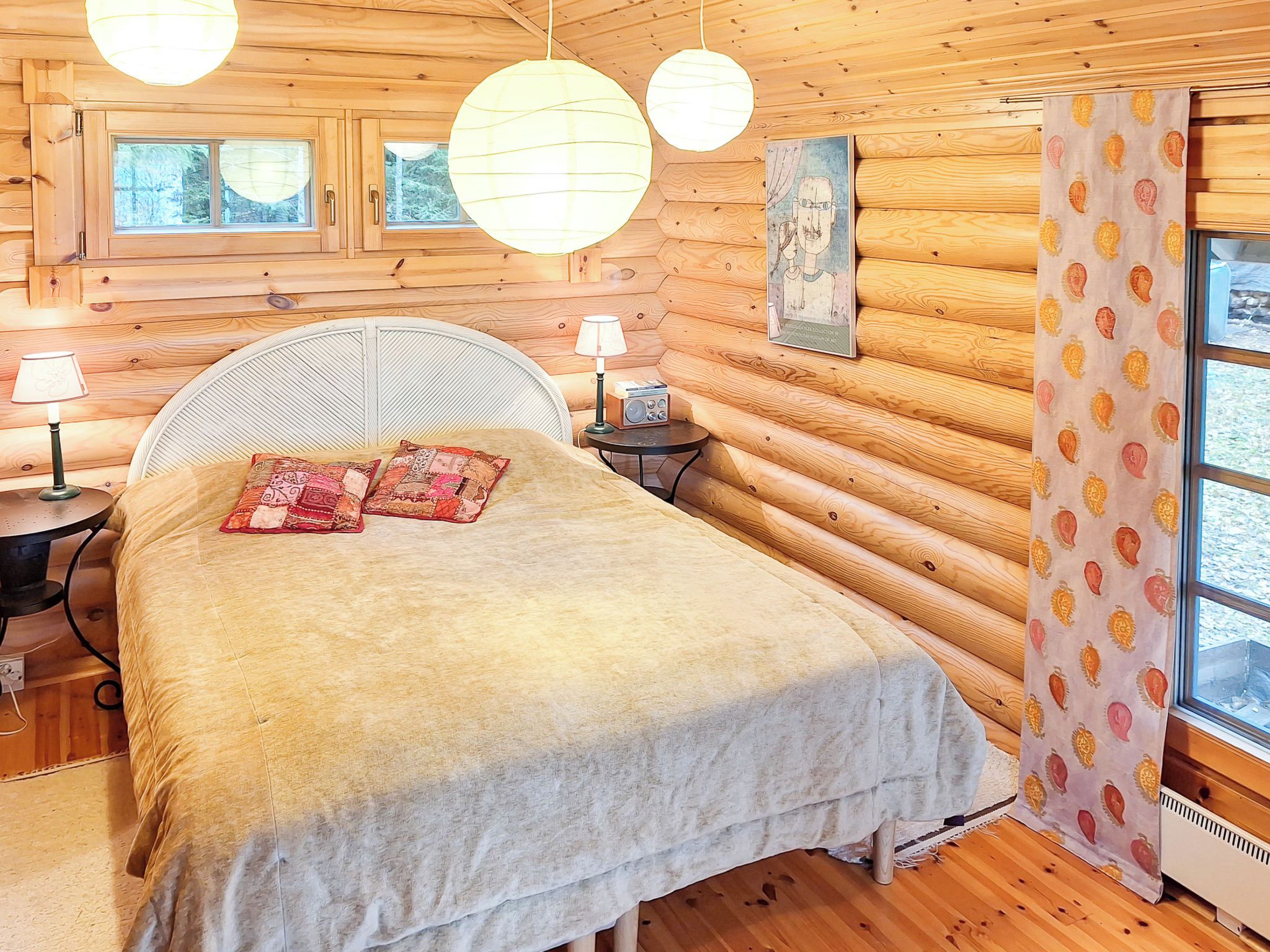 Une chambre à coucher située dans un chalet en rondins, avec un lit, deux lampes, une radio et une fenêtre avec des rideaux.