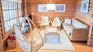 A cozy log cabin interior with a hanging chair, two wicker chairs, a sofa, and a coffee table. - Honkaranta by Interhome (Karstula)
