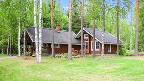 A log cabin with a porch and a chimney, surrounded by a grassy yard and tall trees. - Honkaranta by Interhome (Karstula)