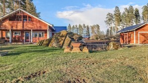 Un chalet rustique doté d’une grande cheminée en pierre, entouré d’une pelouse bien entretenue et de grands arbres.