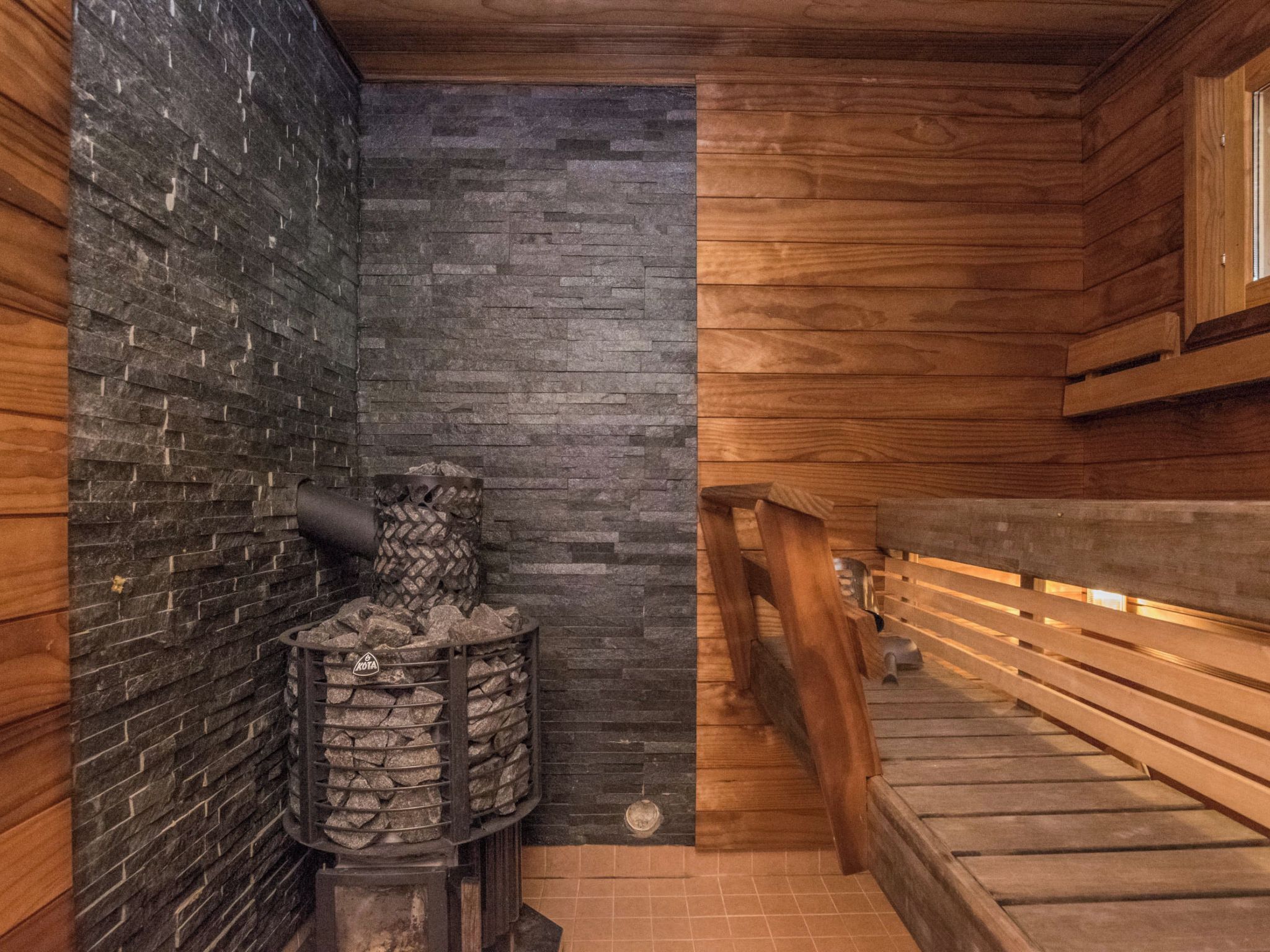 A sauna with a stone wall, wooden benches, and a stone heater.