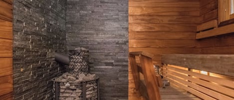 Eine Sauna mit Steinwand, Holzbänken und einem Steinkamin.