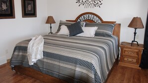 Un dormitorio con una cama, dos mesitas de noche, una obra de arte en la pared y dos fotografías enmarcadas.