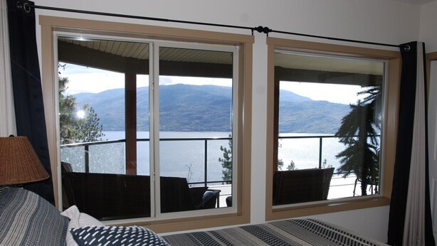Una habitación con una cama, un ventanal con vistas a montañas y un cuerpo de agua, y una silla junto a la ventana.