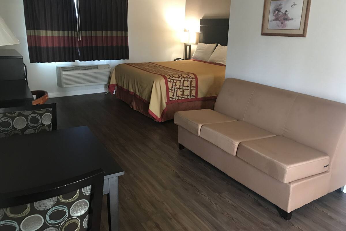 A hotel room with a bed, a sofa, a desk, and a lamp.