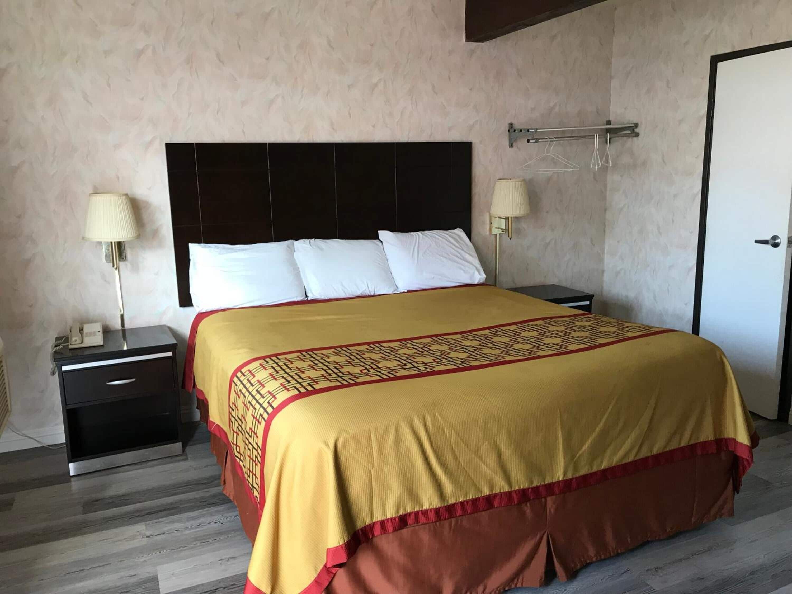 Una habitación de hotel con una cama grande, una mesita de noche con lámpara, un armario y una puerta.