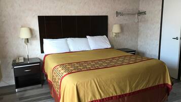 Una habitación de hotel con una cama grande, una mesita de noche con lámpara, un armario y una puerta.