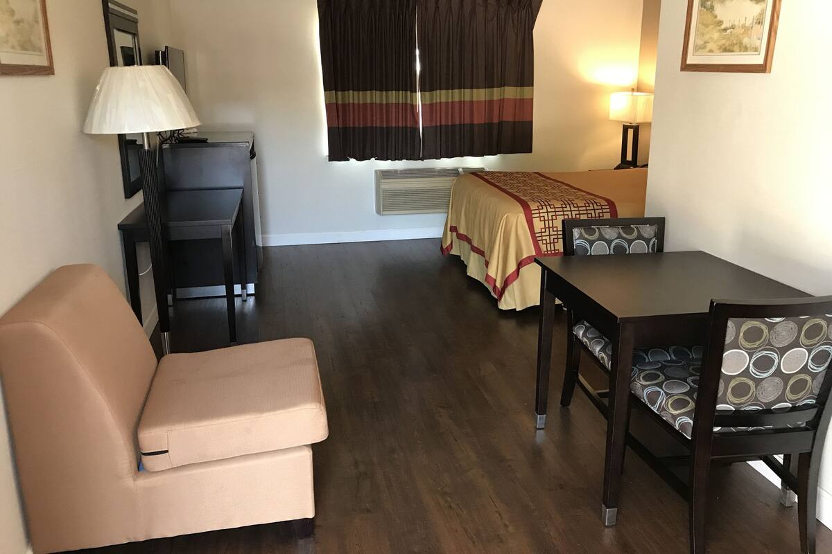 A room with a bed, a desk, a chair, a sofa, and a lamp.