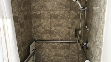 Un espace douche doté d’un sol carrelé, d’une barre d’appui, d’un pommeau de douche à main et d’un porte-serviettes.