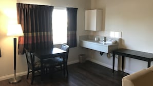 A small, clean room with a dining table, chairs, a lamp, a sink, and a mirror.