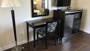 A compact room with a desk, chair, TV, and a small kitchenette.