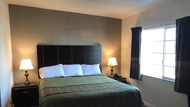 A hotel room with a bed, two bedside lamps, a telephone, a window with curtains, and a dark headboard.