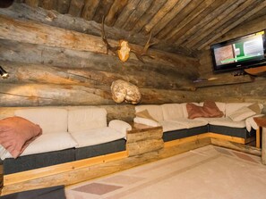 L'intérieur d'une cabane en rondins, avec un canapé et un téléviseur fixé au mur.