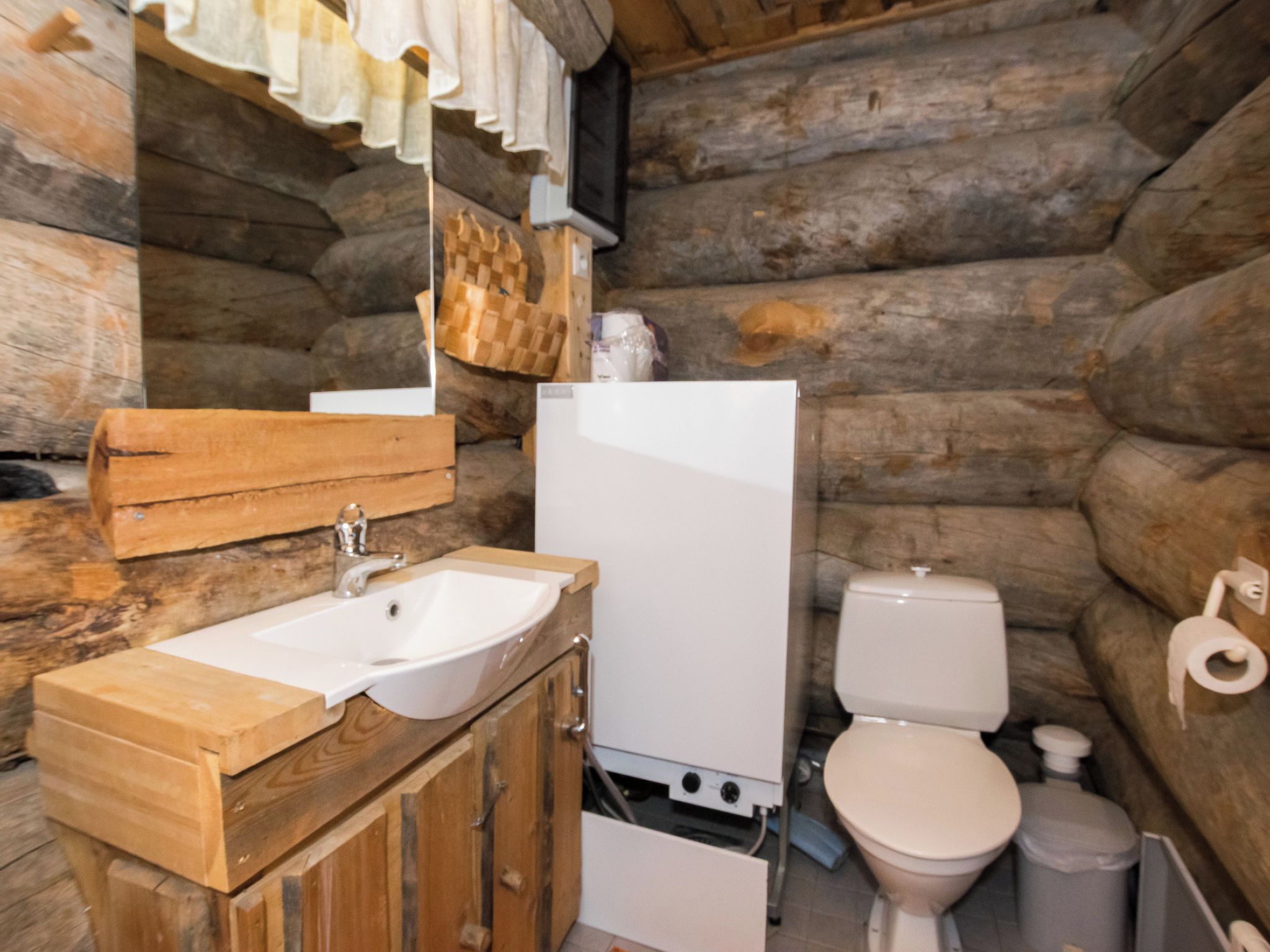 Baño de cabaña de troncos con lavamanos de madera, inodoro blanco y espejo sobre el lavamanos.