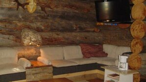 Ein rustikales Interieur mit einer Holzwand aus Baumstämmen, einem weißen Sofa, einem Couchtisch und einem an der Wand befestigten Flachbildfernseher.